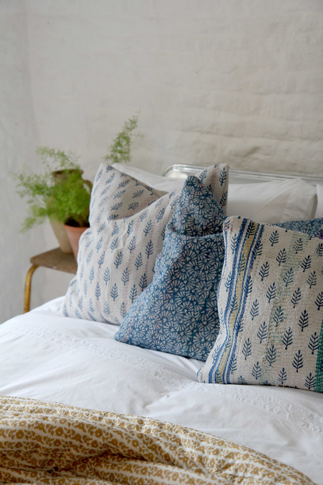 vintage white and blue block print sari cushions scattered on bed with ochre coloured quilt and white bed linen