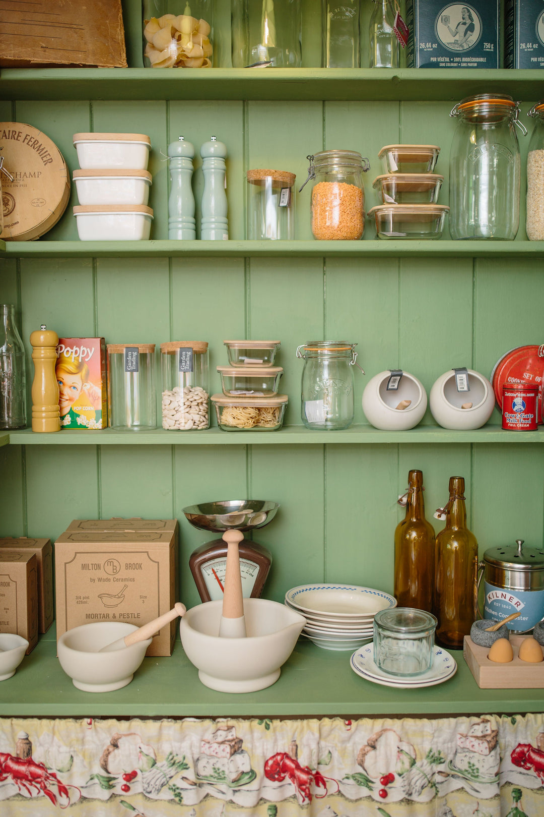 green kitchen pantry shelves with jars, bottles and enamelware