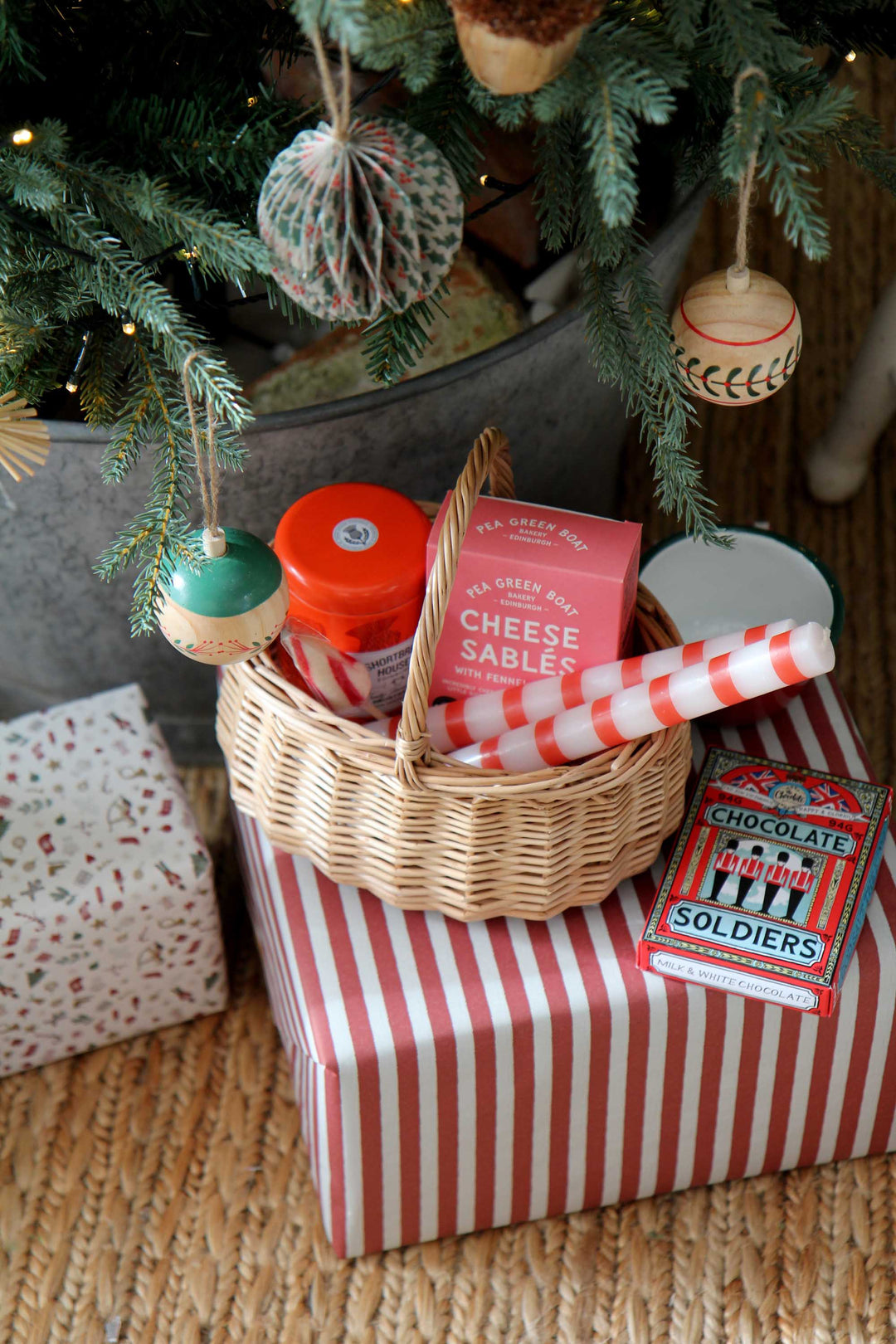 Basket with Christmas-themed items on a striped box under a decorated tree