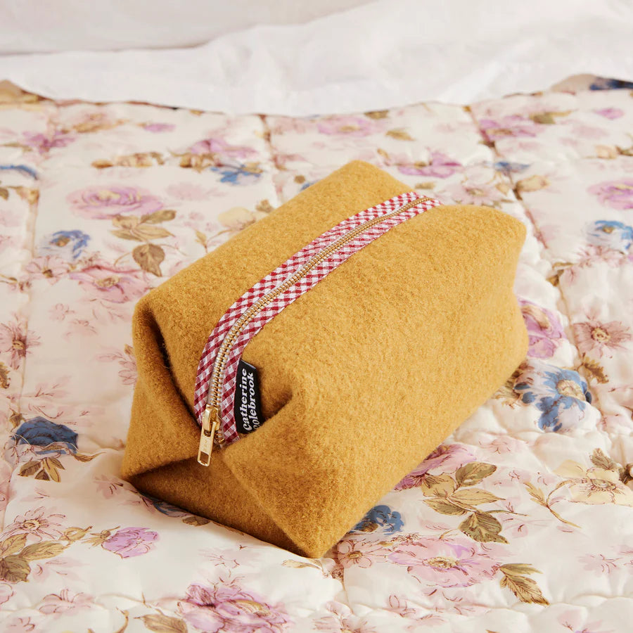 Mustard-colored pouch with a red and white checkered zipper on a floral blanket