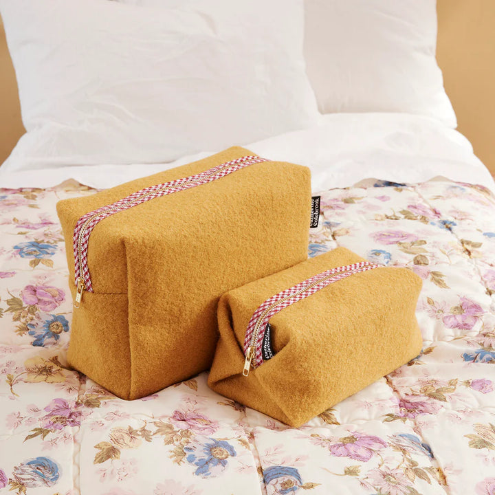 Two mustard-colored wedge pillows with braided straps on a floral bedspread.
