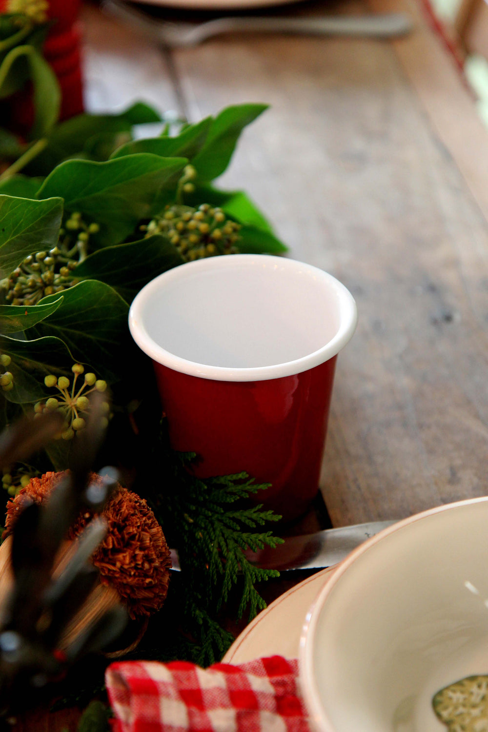 burgundy falcon enamelware cup on a table with greenery and a checkered cloth