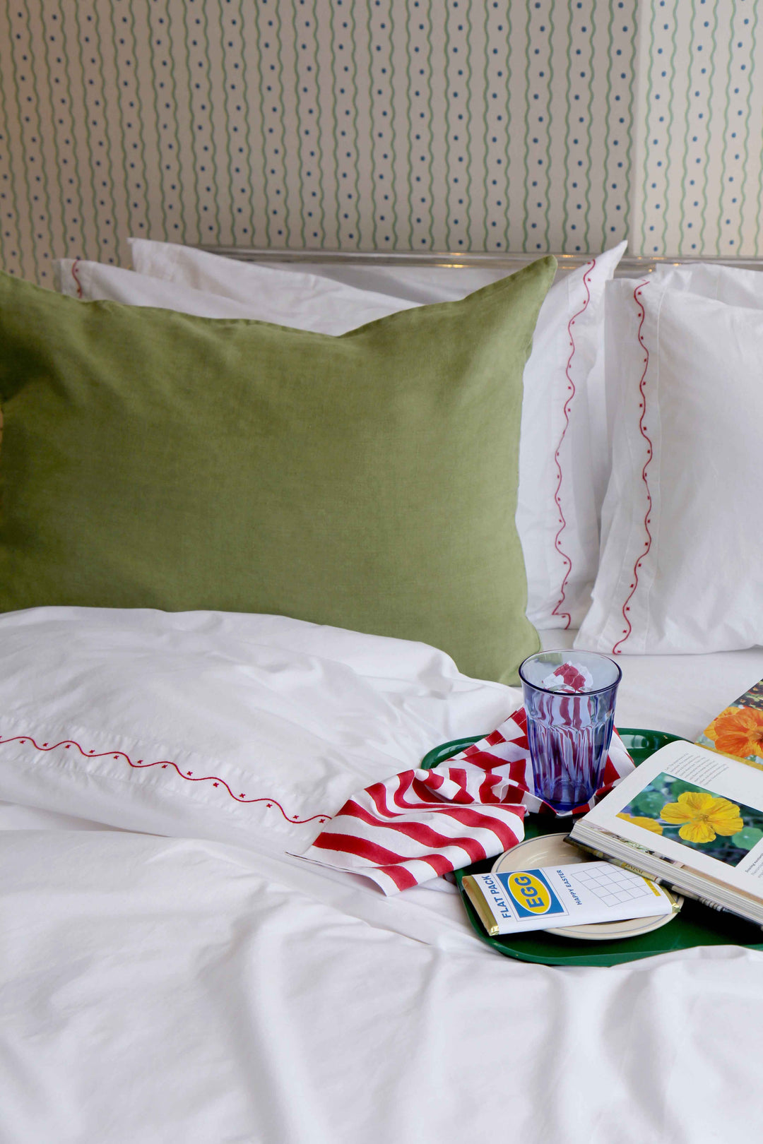 lifestyle image of domestic science criss-cross bedding in poppy red with morning drinks tray and book