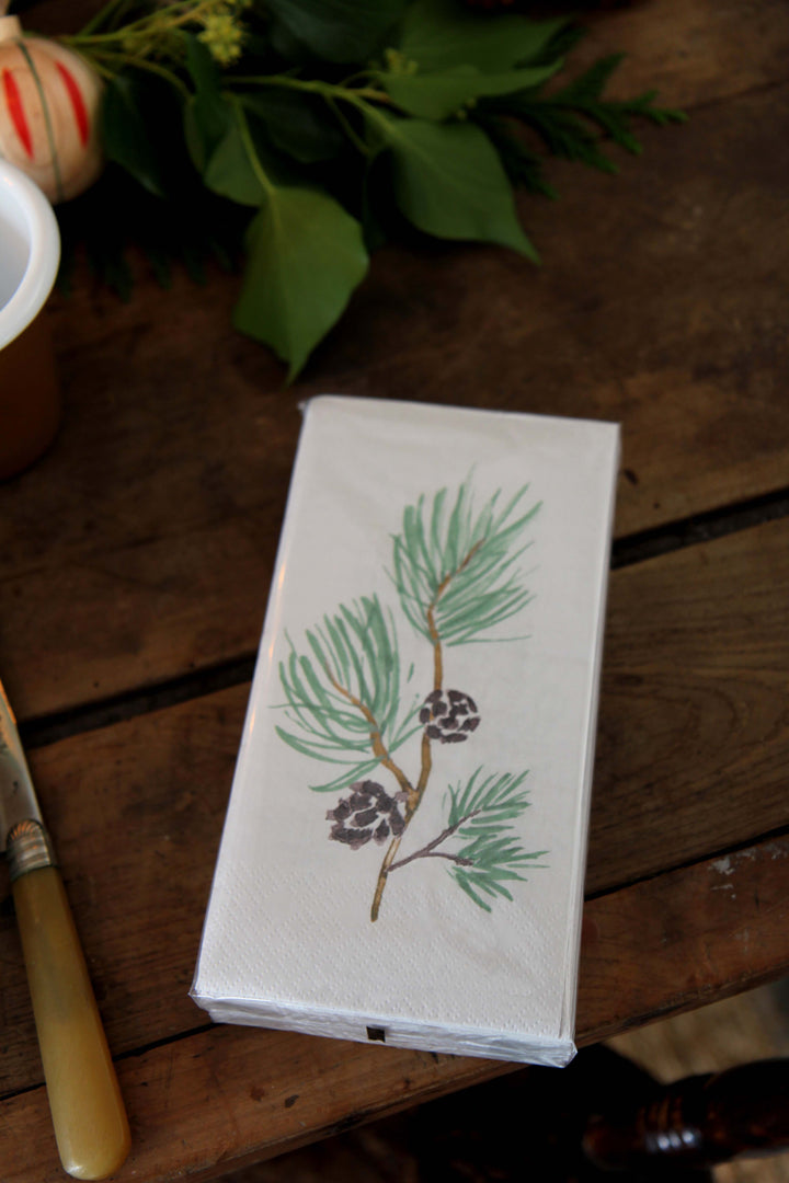 Paper napkins with pine branch and pine cone design on a wooden surface