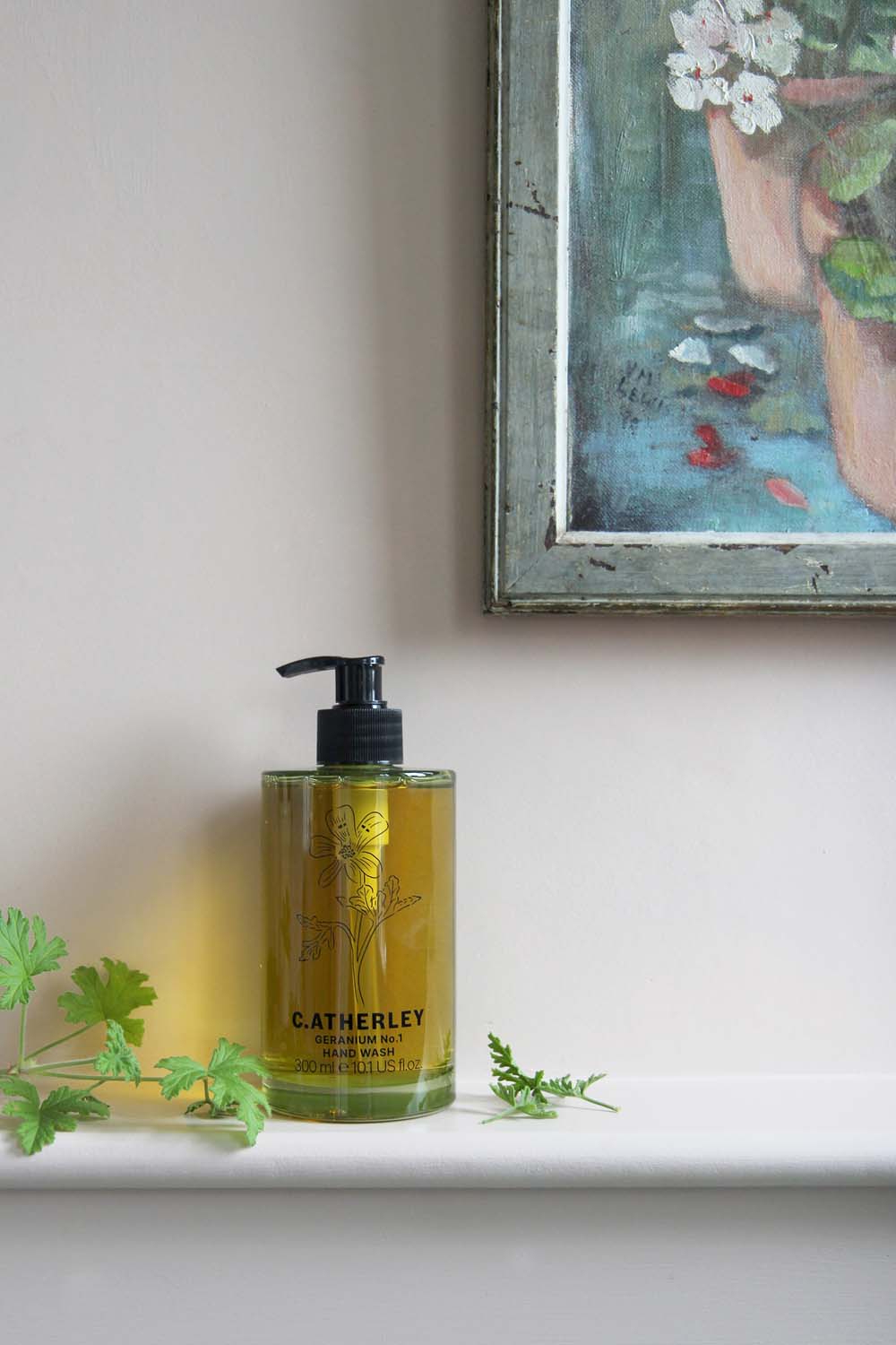 c.atherley geranium hand wash in green glass bottle in pink bathroom with geranium leaves