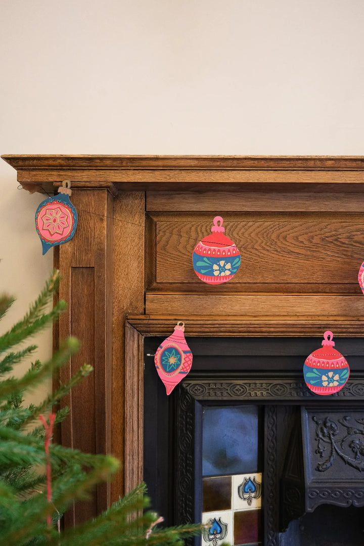 Decorative Christmas ornaments on a wooden mantelpiece with a fireplace in the background.
