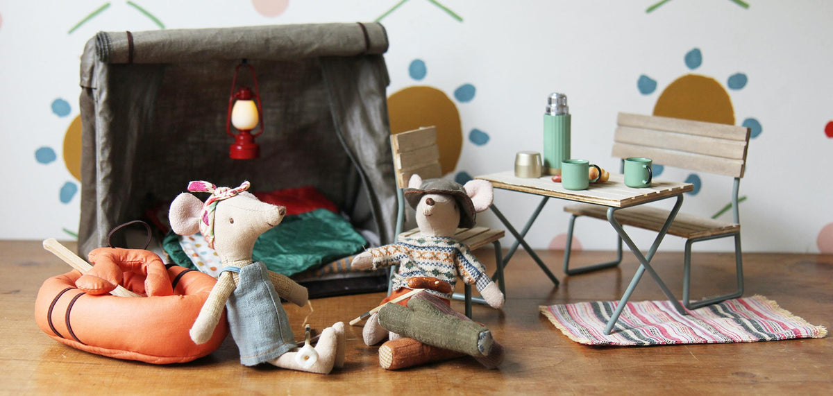 Toy mouse characters in a camping scene with a fireplace, table, and chairs.