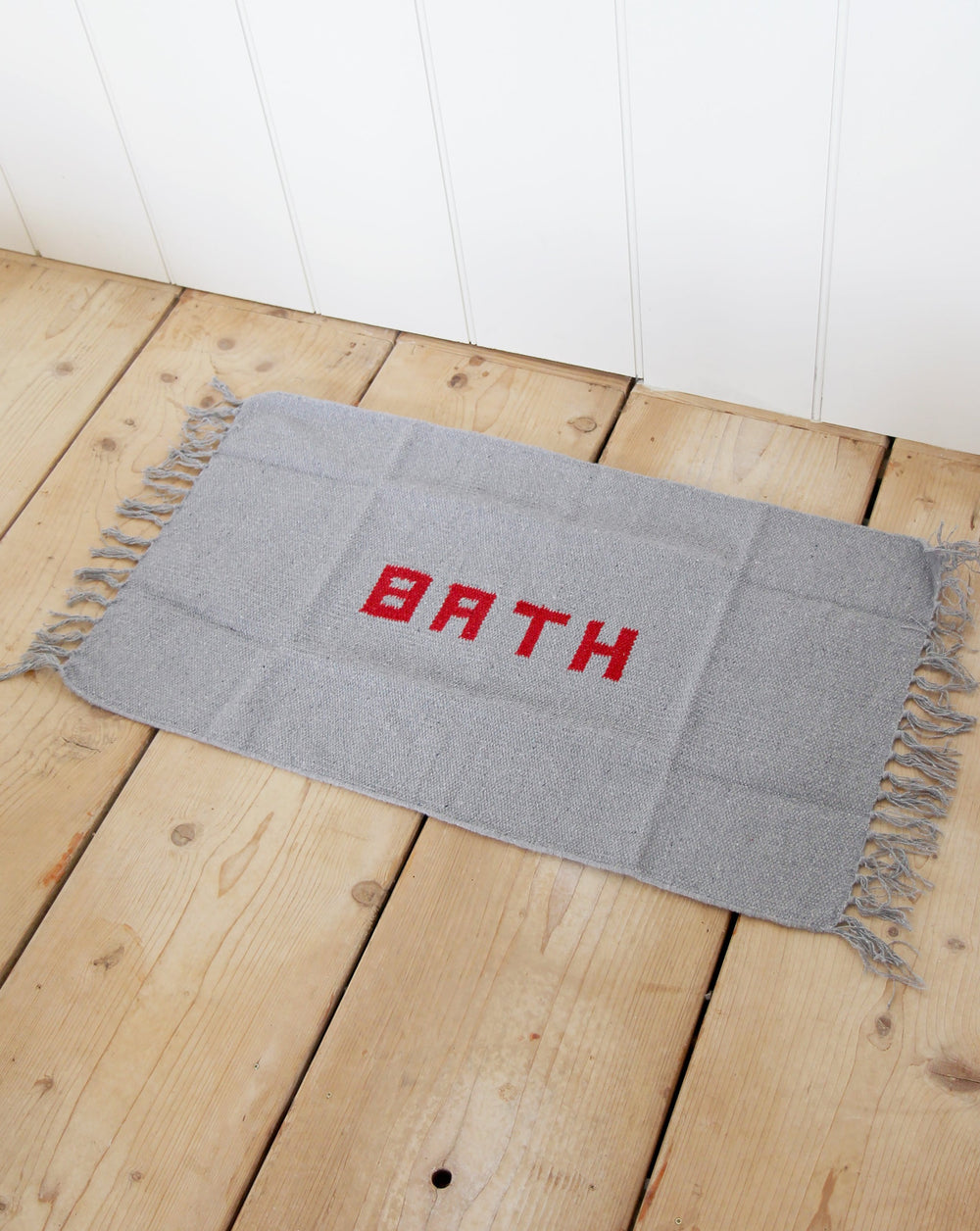 puebco grey woven bath mat with red word BATH on reclaimed antique pine floorboards