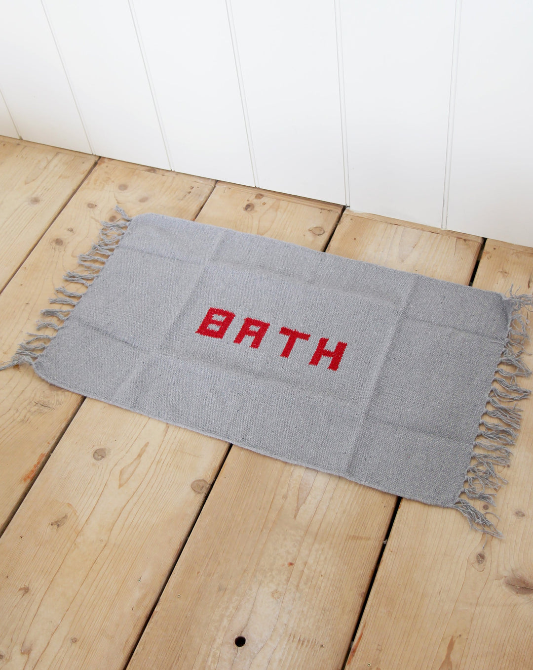 puebco grey woven bath mat with red word BATH on reclaimed antique pine floorboards