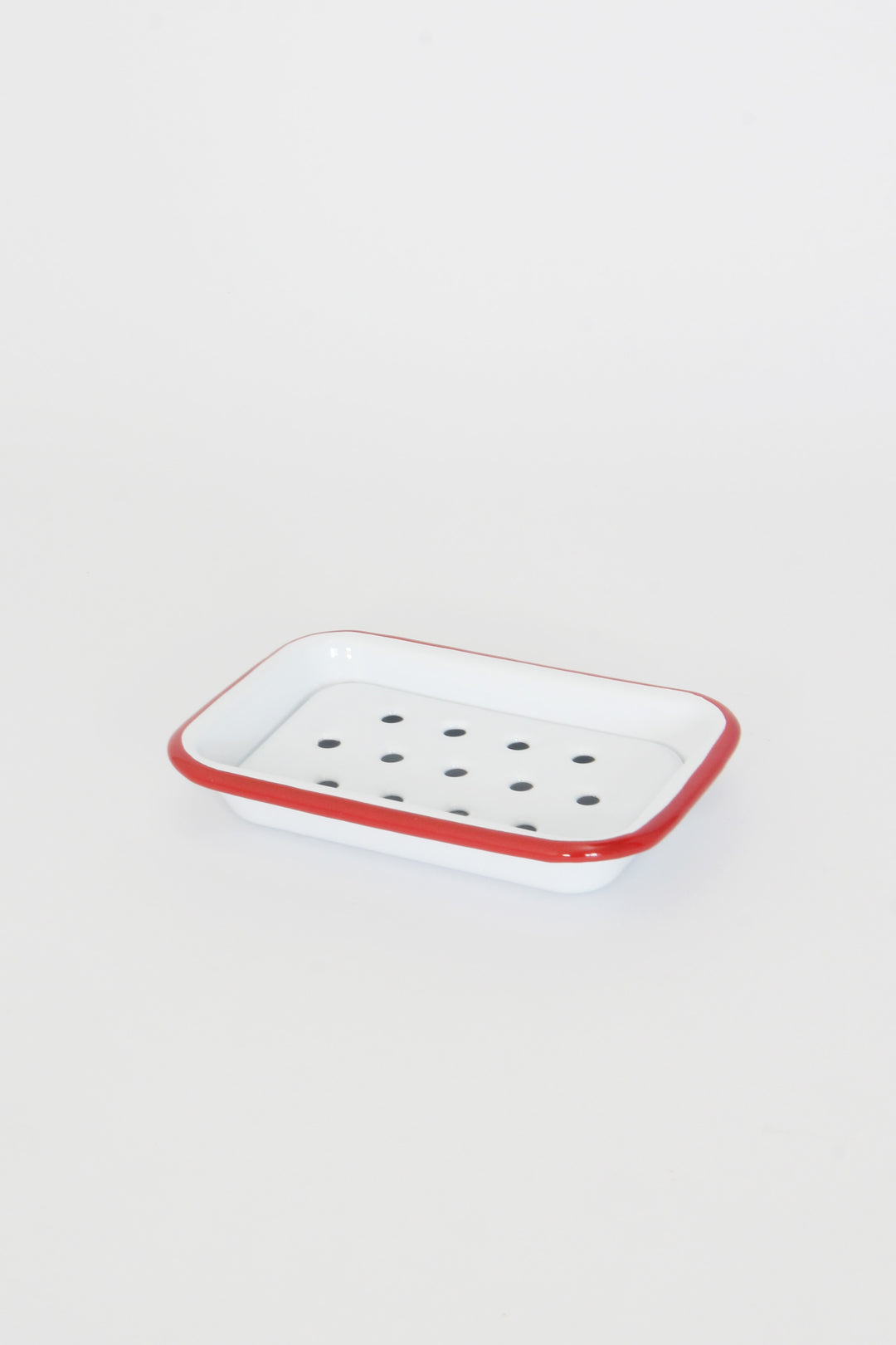 A white enamel soap dish with red trim and draining holes, placed on a plain background.