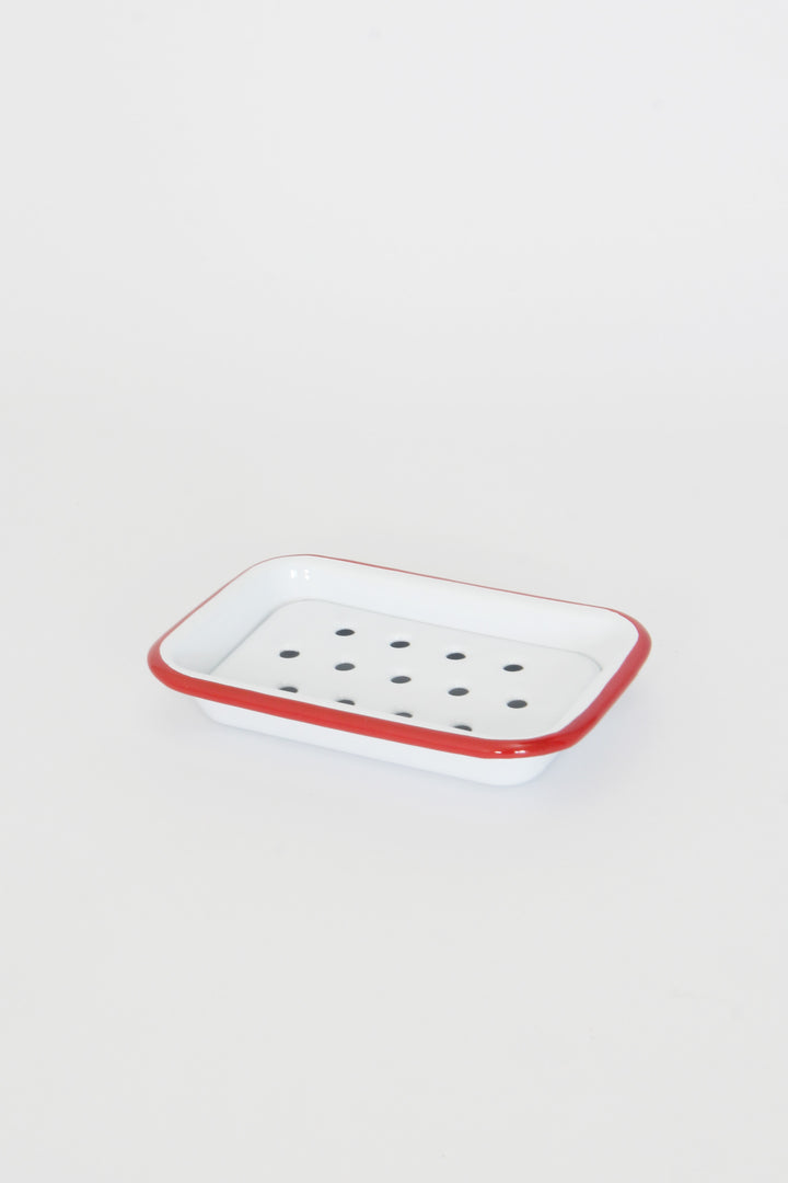 A white enamel soap dish with red trim and draining holes, placed on a plain background.