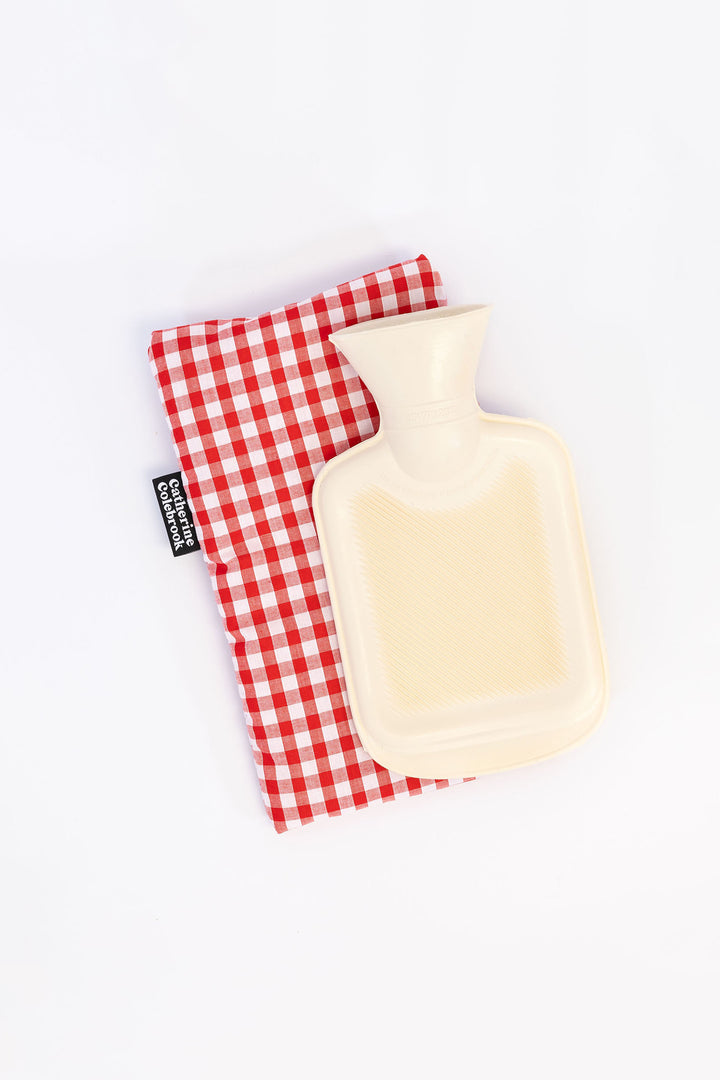 A beige hot water bottle with a red and white checkered cotton cover.