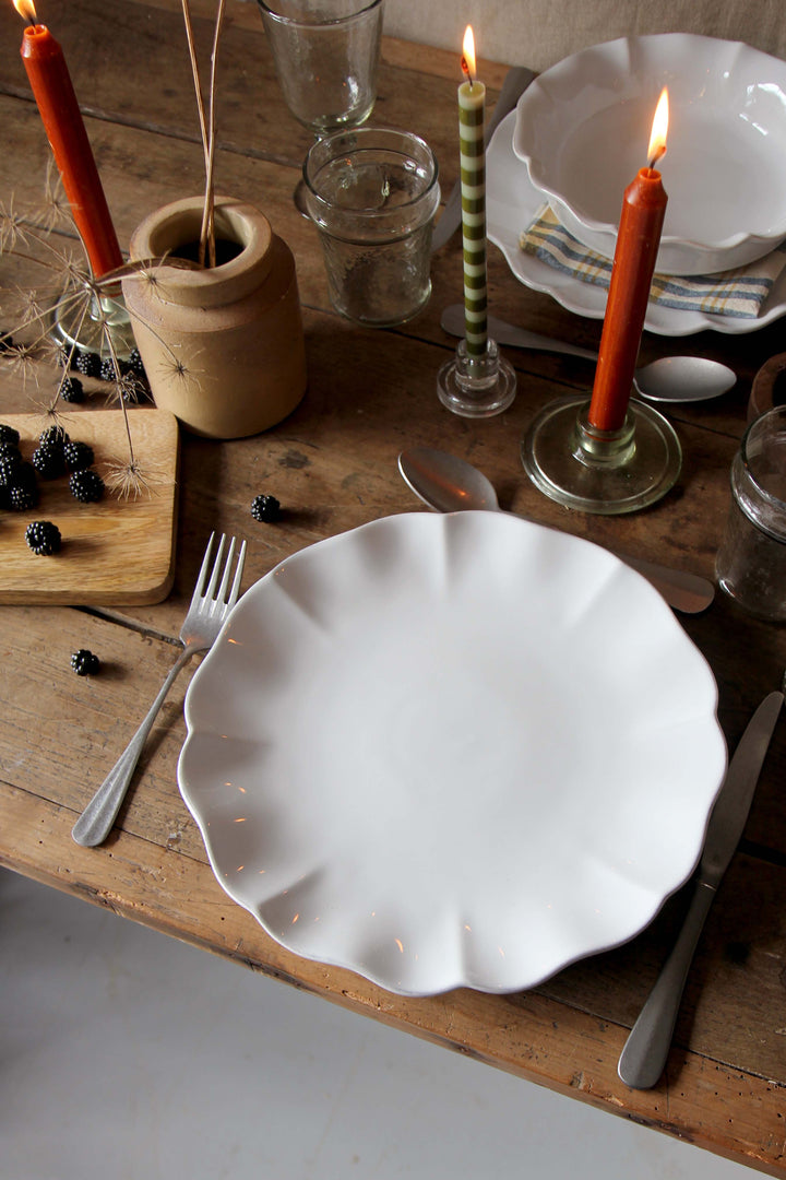 Dining table setting with white plates, candles, and cutlery on a wooden surface.