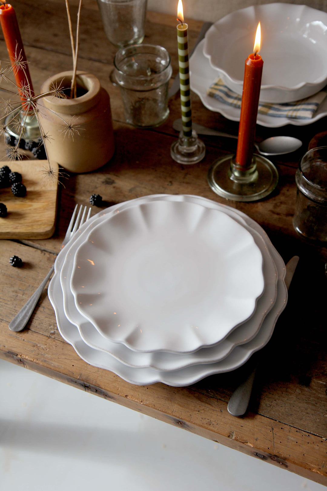 Stack of white ceramic plates on a wooden surface with candles and jars in the background.