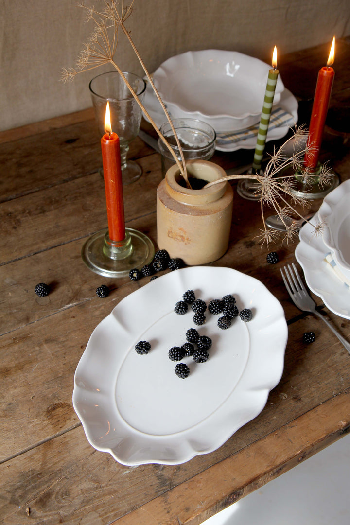 Dinner table setting with white scalloped platter, blackberries, and lit candles on a wooden surface.