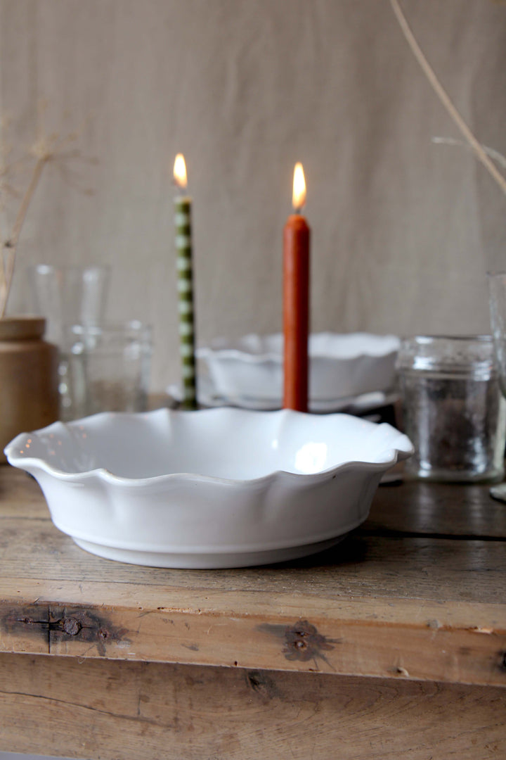 White rosa scalloped pasta plate on a wooden surface with candles and glasses in the background