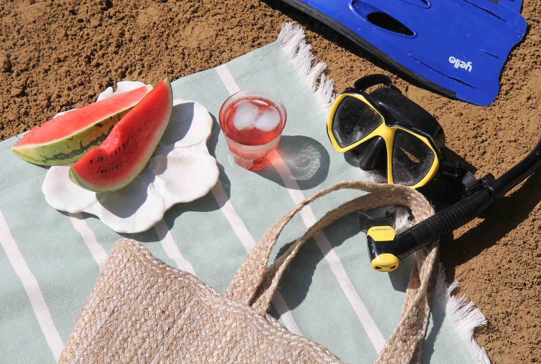 striped beach towel, jute beach bag, snorkel, summer drink and watermelon