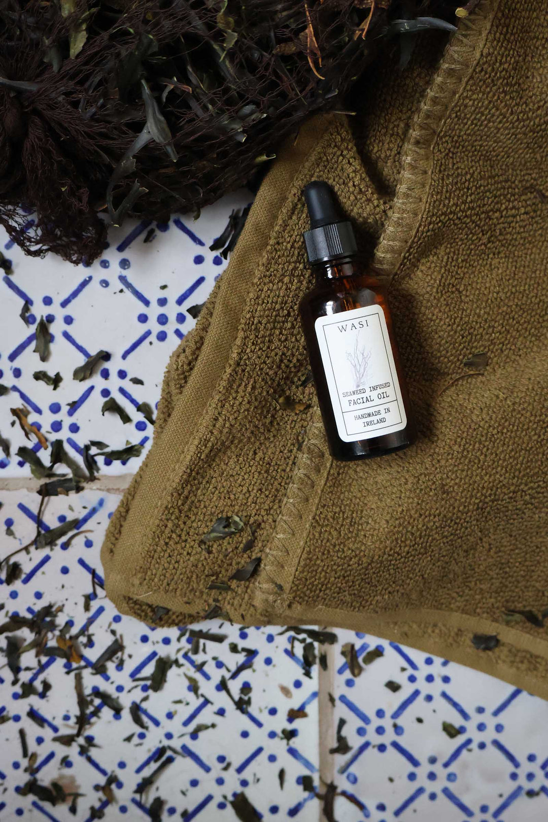 wasi seaweed face oil on olive green towel and vintage spanish blue and white towels