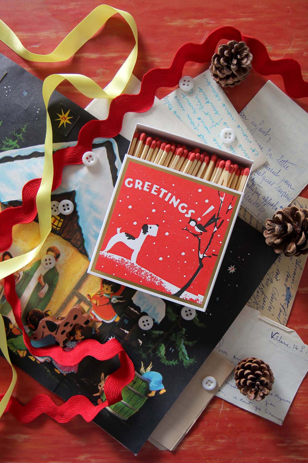 box of luxury winter greetings matches, red box with dog motif, against a backdrop of festive ribbons and trims