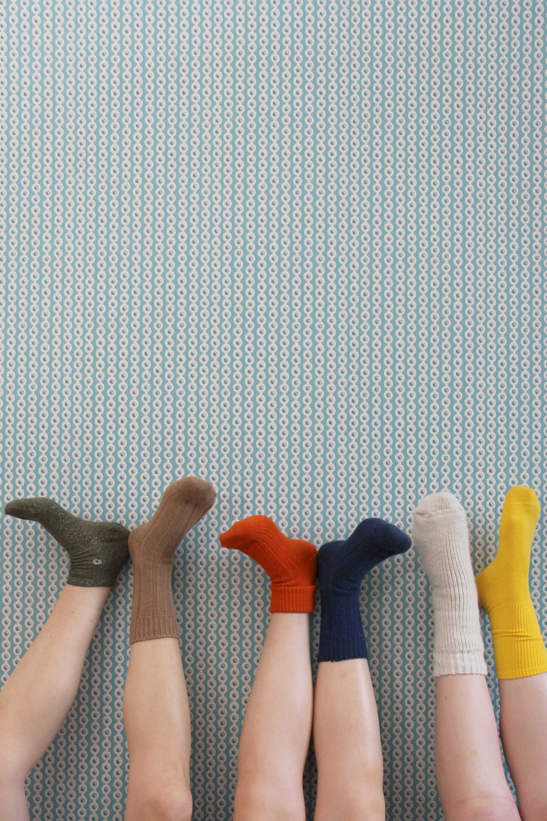 3 pairs of legs showcasing colourful socks against a patterned wall - Domestic Science Home