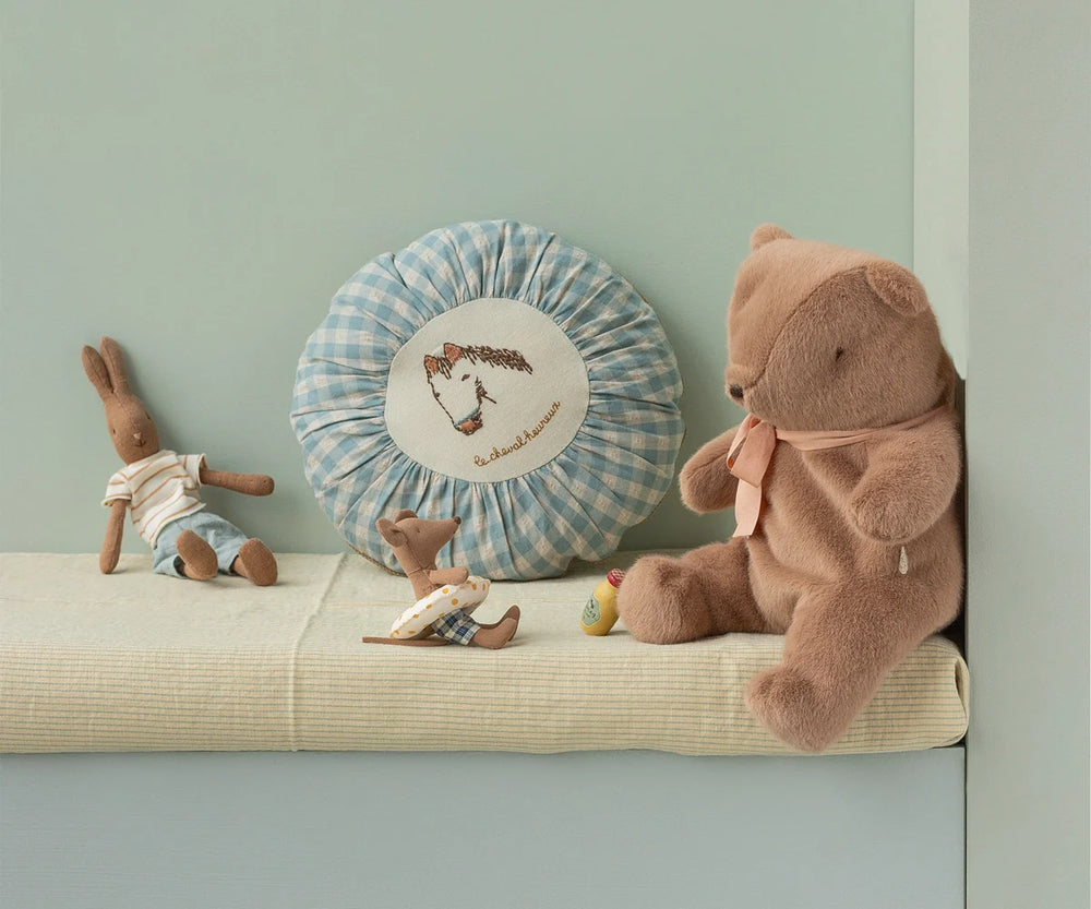 Children's toys including a teddy bear and rabbit on a cushion against a light green wall with a decorative pillow.