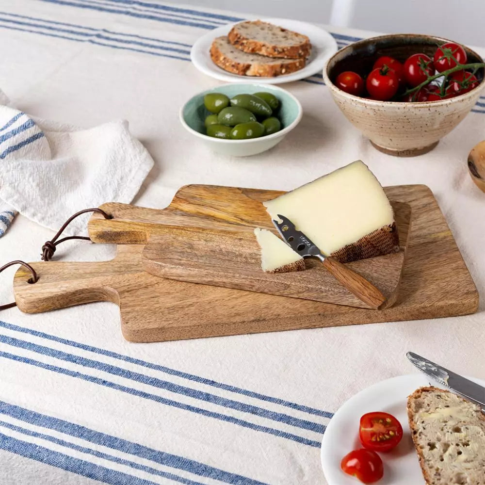 Wooden cutting boards with cheese and bread on a tablecloth with bowls of olives and tomatoes.