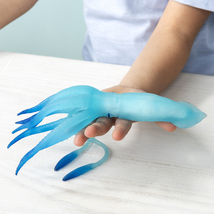 Person holding a blue squid-shaped toy on a white surface