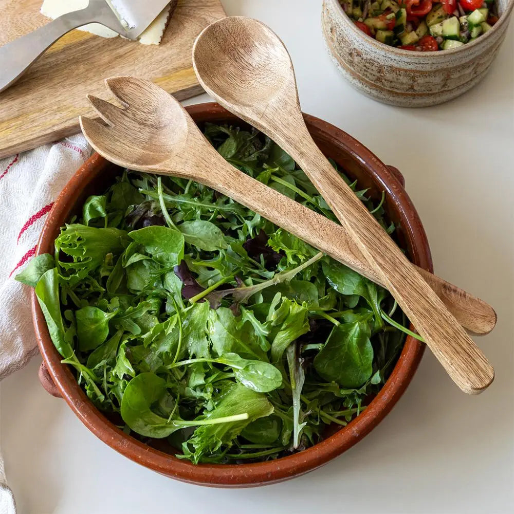 Bowl of green salad with wooden utensils on a white surface