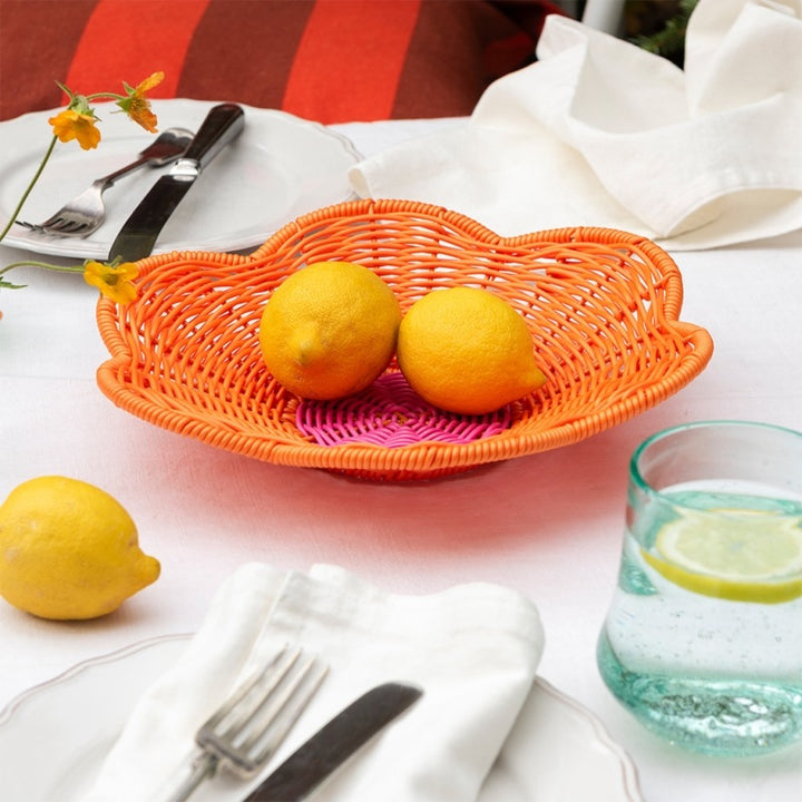 Orange basket with lemons on a table with cutlery and a glass of water.