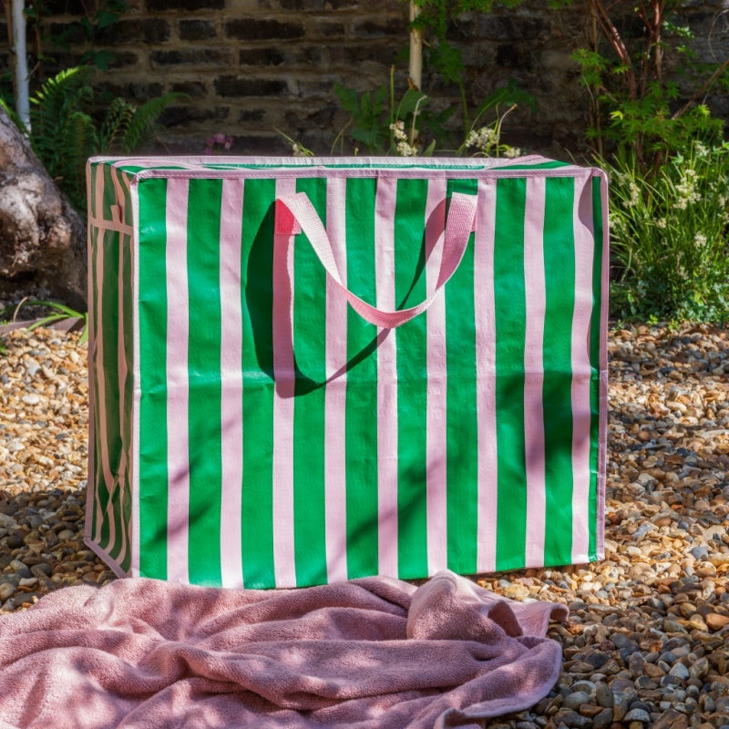 Green and pink striped bag with a monogram on a gravel surface with plants in the background