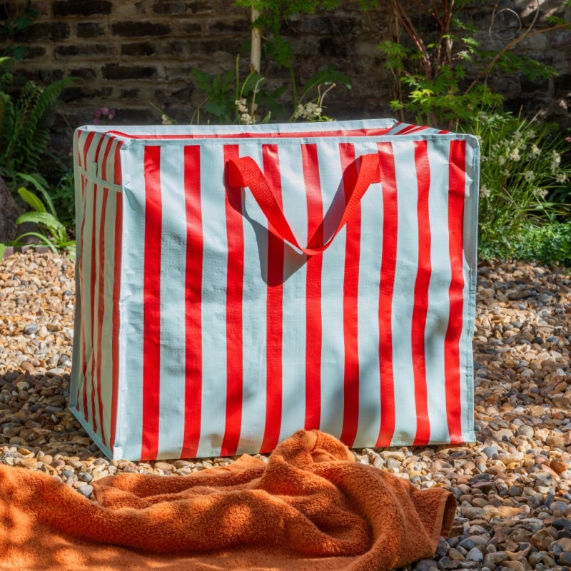 Red and white striped storage bag on pebbles with an orange towel in front