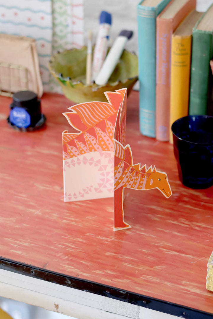 Dragon card on a wooden surface with books and stationery items in the background