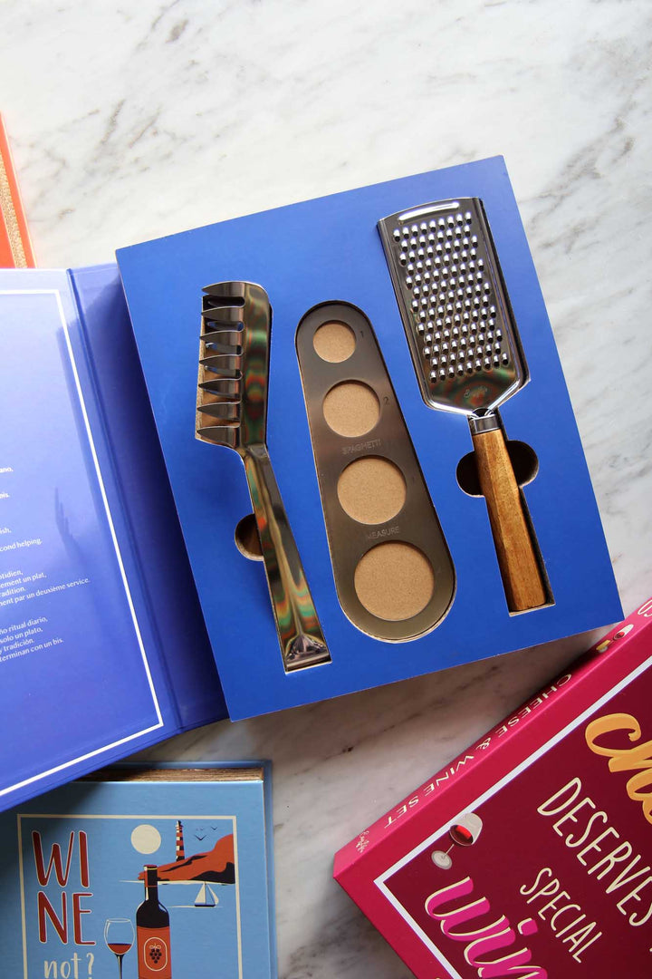 Set of kitchen tools including a grater and spatula in a blue box on a marble surface.