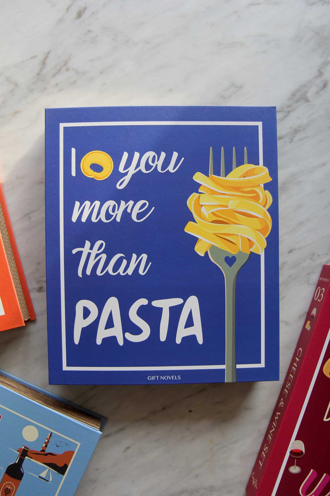 Card with 'I love you more than pasta' text and a fork with pasta on a marble surface.