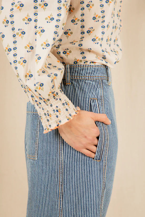 Person wearing a floral blouse and blue striped pants against a beige background