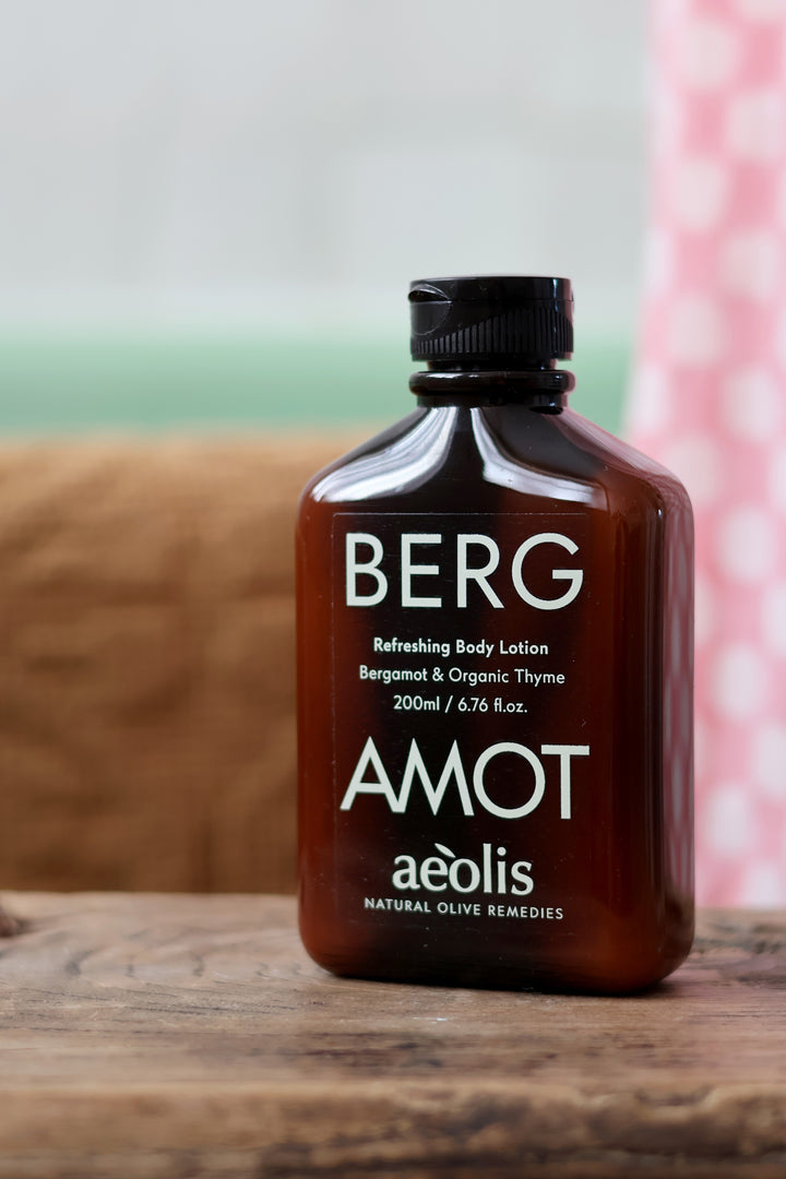 A bottle of Berg Amot aéolis natural olive remedies refreshing body lotion, in an amber brown bottle with a black cap, set on a rustic wooden surface.
