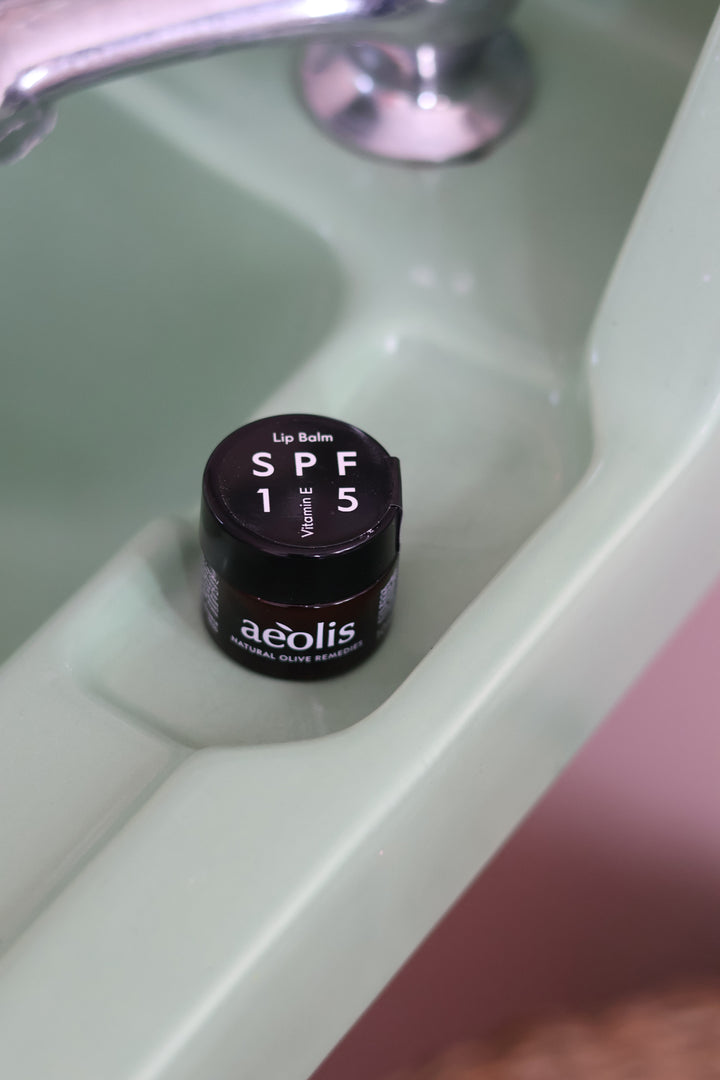 A small jar of aeolis Lip Balm SPF 15 in shade E, placed inside a pale green ceramic sink basin.
