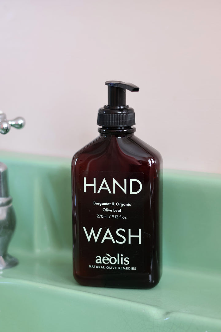 A bottle of aèolis hand wash in a dark amber bottle with a black pump dispenser, placed on a mint green sink next to a chrome faucet.