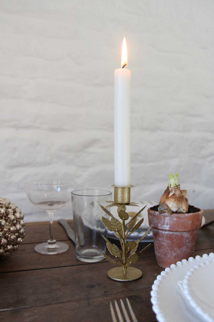 Candle on a gold candlestick with decorative elements on a wooden table.
