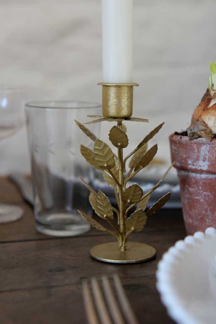 Gold leaf candle holder with a white candle on a wooden table.