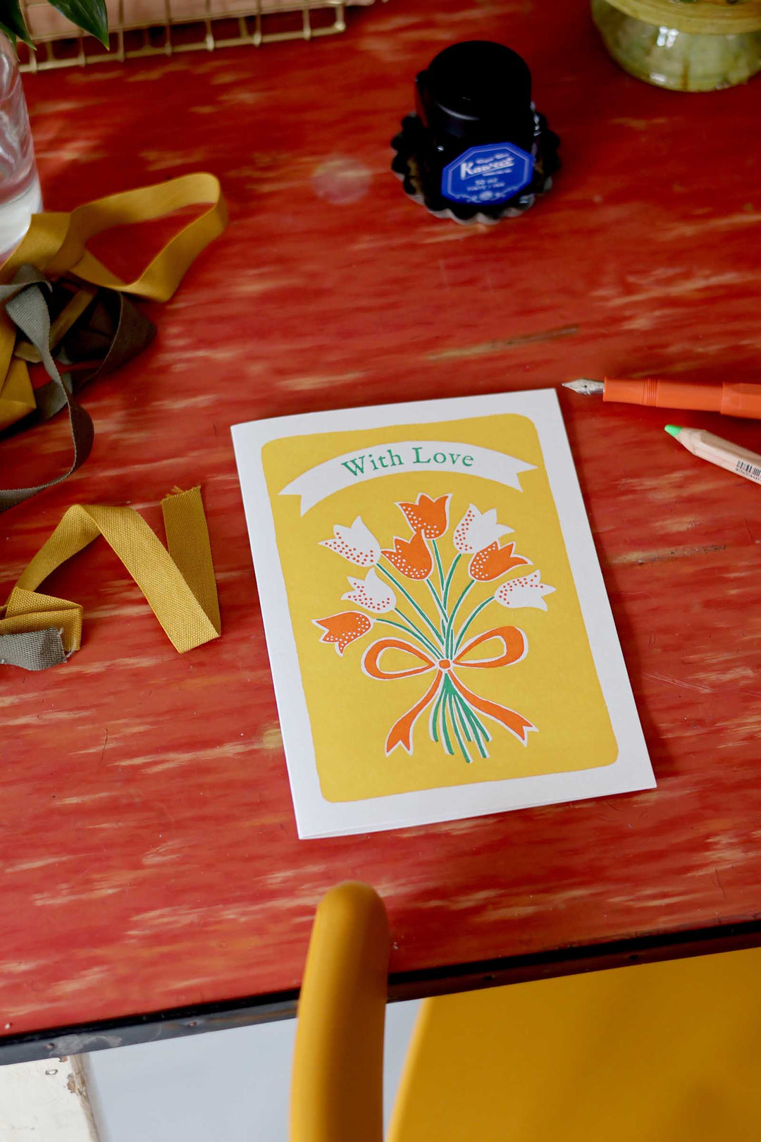 Card with floral design and 'With Love' text on a red surface with ink bottle and markers.