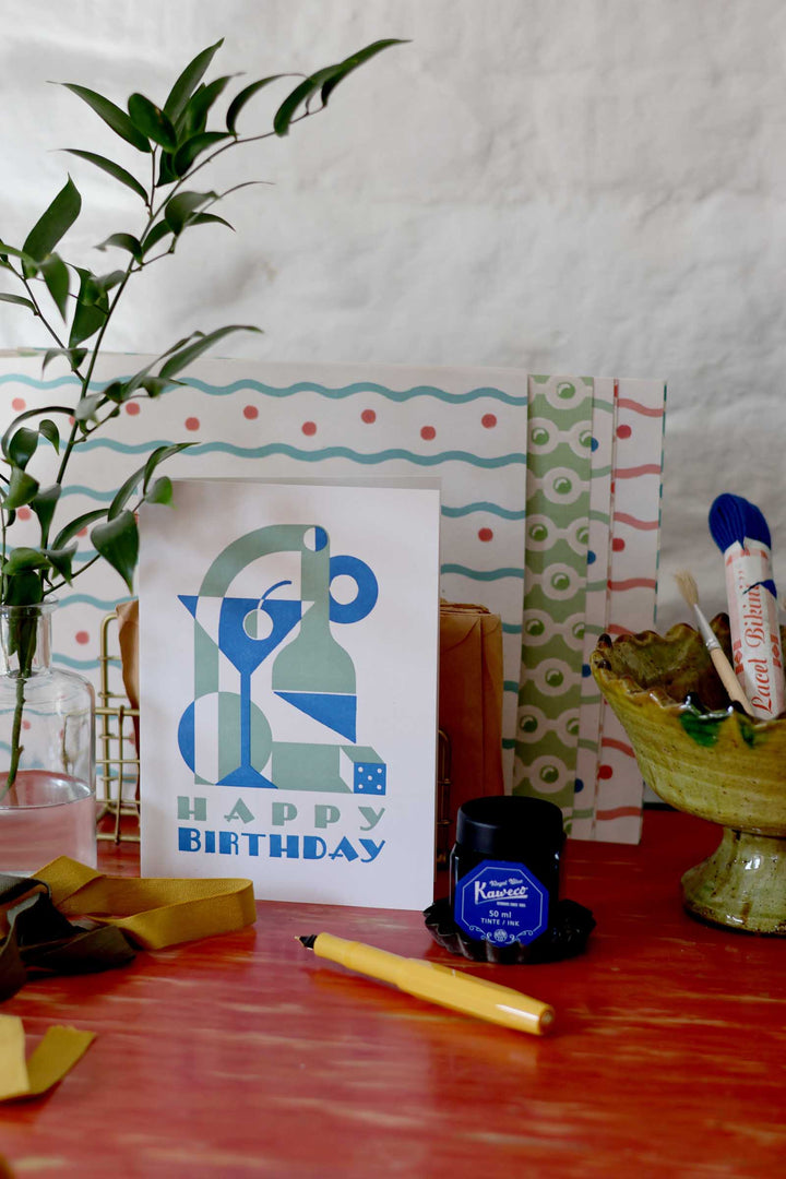 Birthday card with blue and green design on a table with stationery items