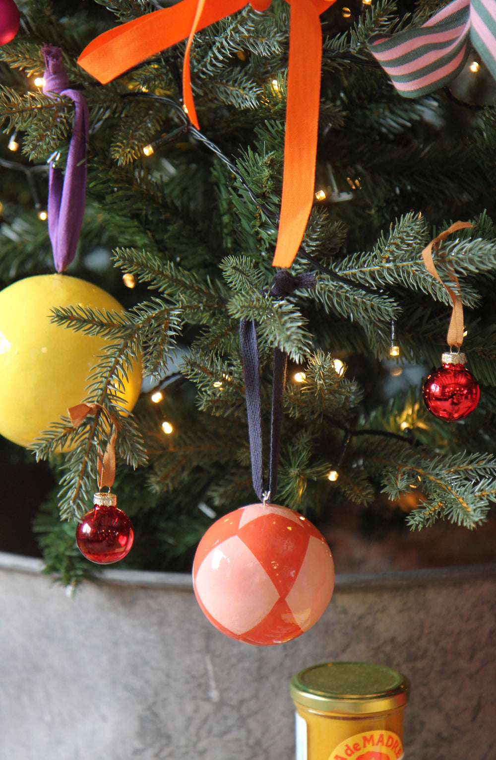 Colorful Christmas ornaments on a decorated tree with a jar in the foreground.