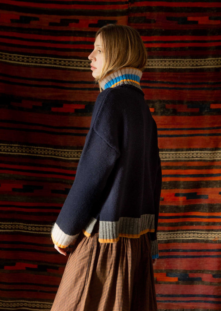 Person wearing a dark sweater with a colorful collar against a patterned wall.