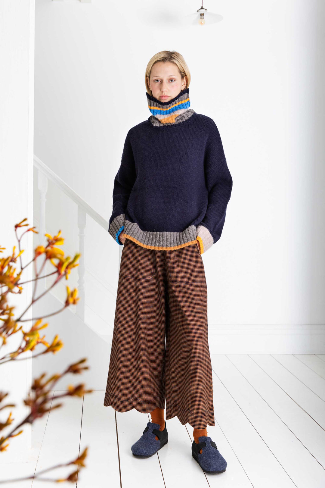 Person wearing a navy sweater and brown pants in a minimal indoor setting