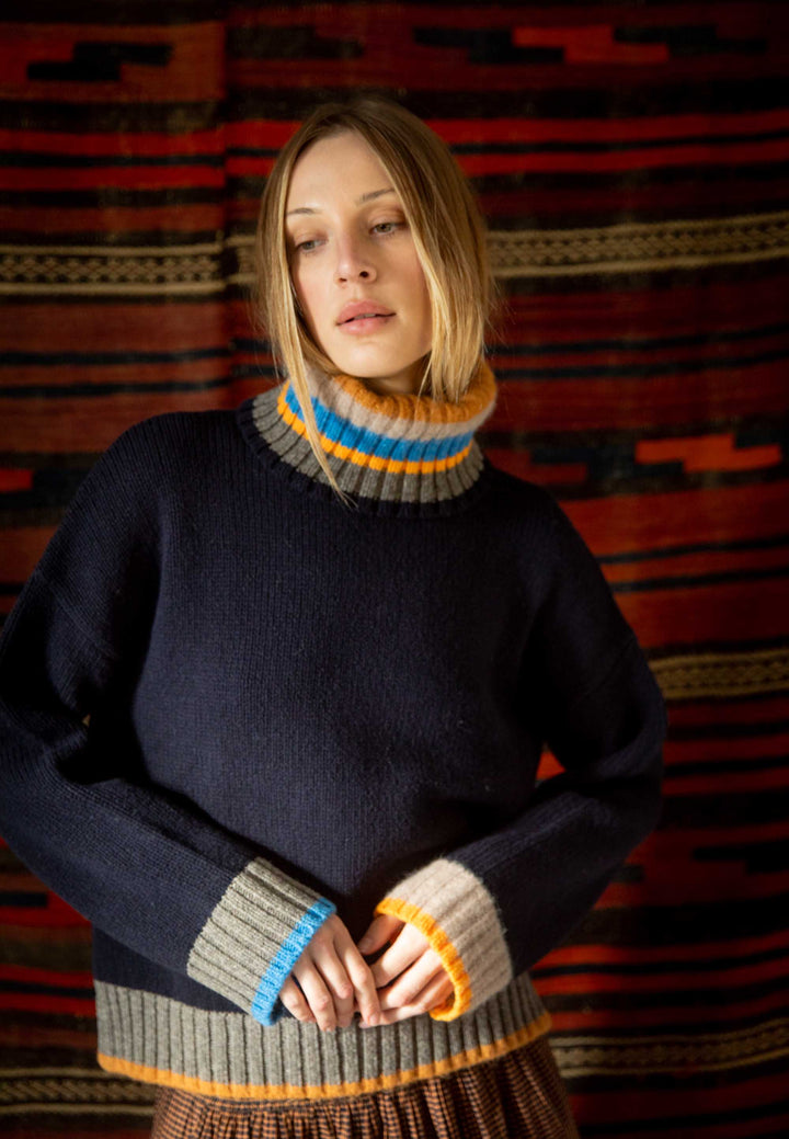 Woman wearing a dark sweater with multicolored cuffs and collar against a patterned background