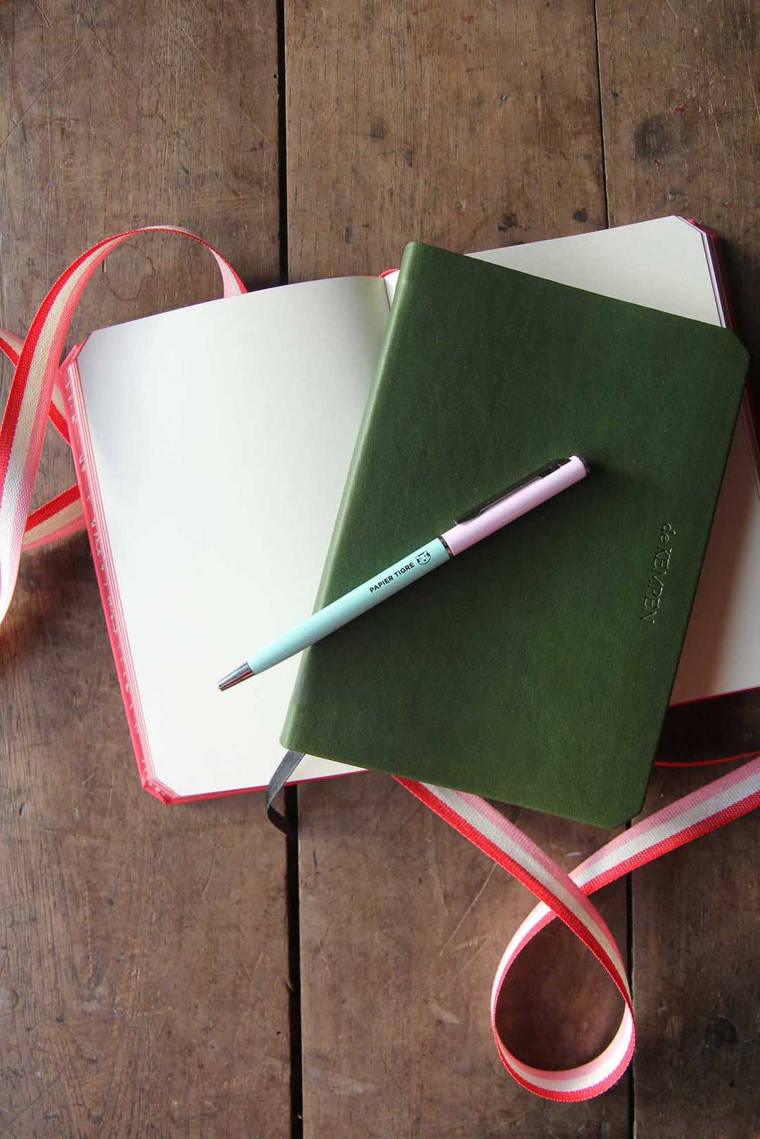 Green notebook with a pink pen on a wooden surface