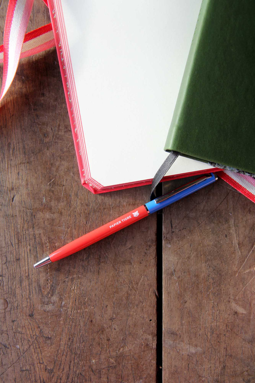 Red pen with blue clip on a wooden surface next to an open book