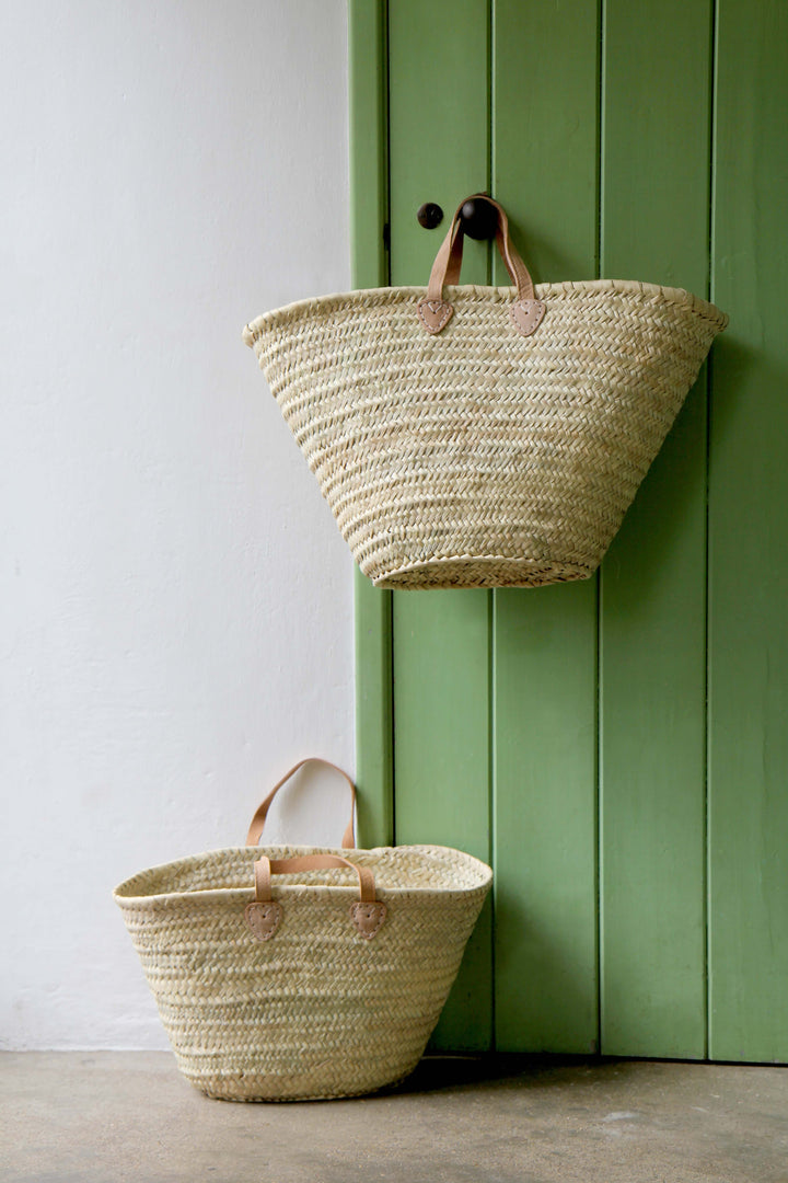 Two woven baskets against a green door and white wall.