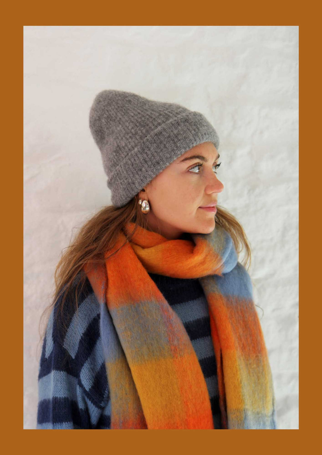 Woman wearing a gray knit beanie and colorful plaid scarf against a white background